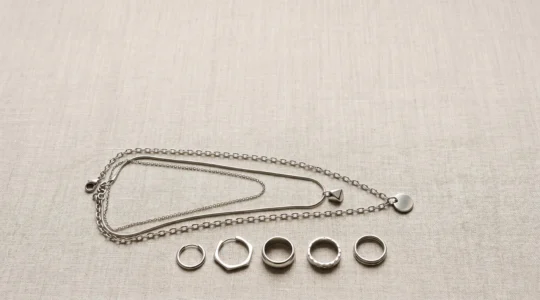 Composición minimalista de joyería en acero quirúrgico con collares superpuestos y pendientes sobre fondo neutro con espacio negativo