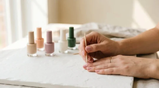 Manos aplicando diseño de nail art con herramientas caseras sobre fondo minimalista